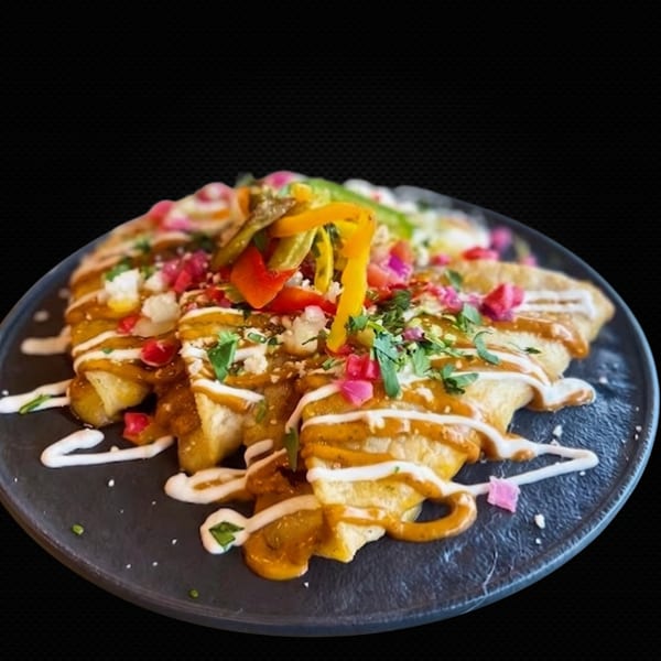 Enchiladas topped with colorful peppers, cilantro, and white sauce on a dark plate.